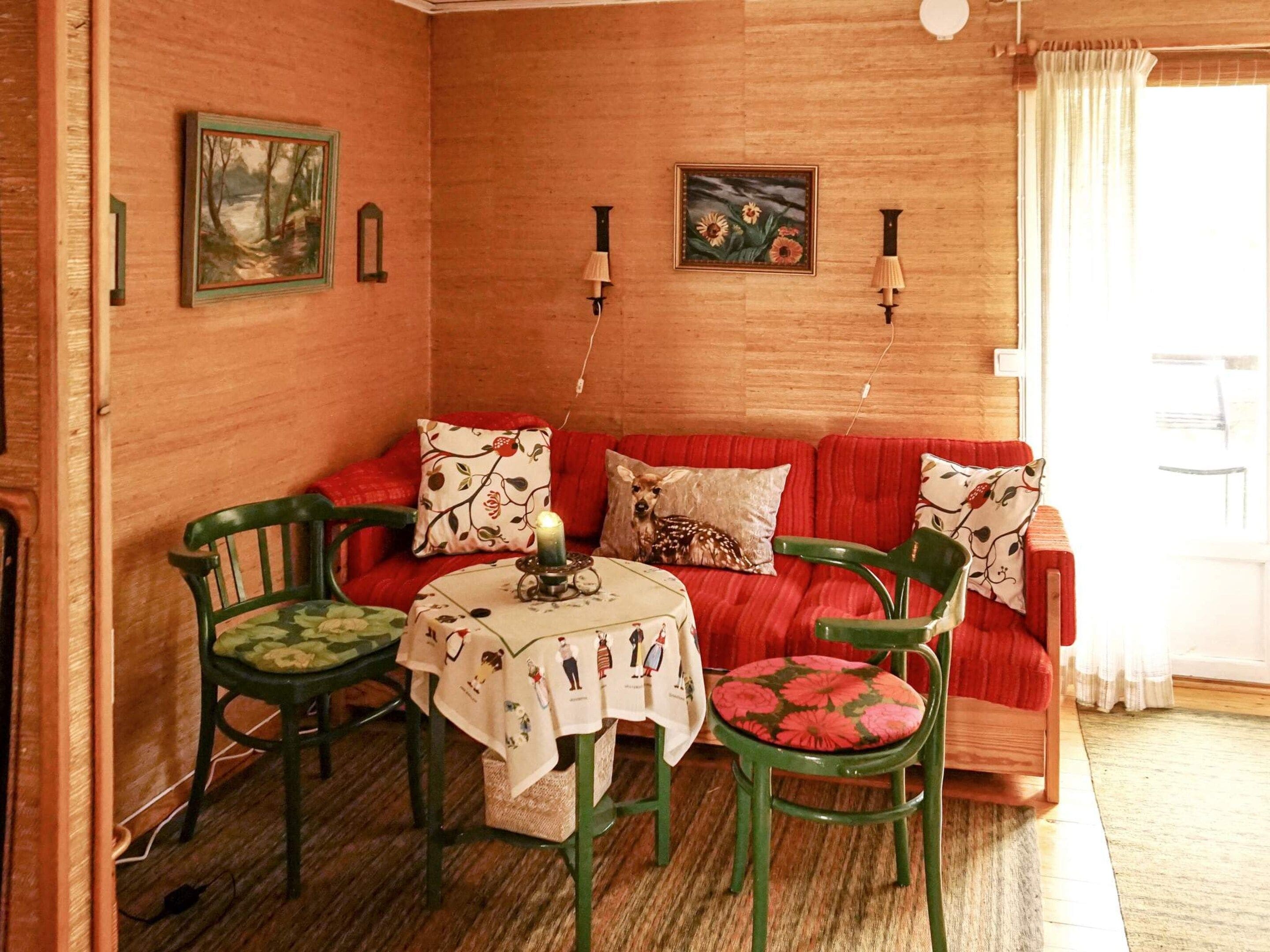 Een gezellige kamer met een rode bank, twee groene fauteuils, een klein tafeltje met een kaars en wandlampen.