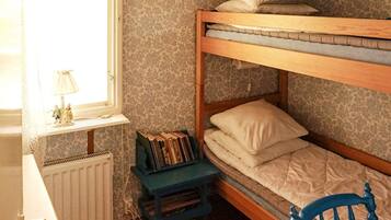 A bunk bed with a lower bunk, a small table with books, a window with a lamp, and a radiator.