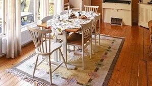 Un comedor acogedor con una mesa de madera, sillas blancas y un mantel estampado.