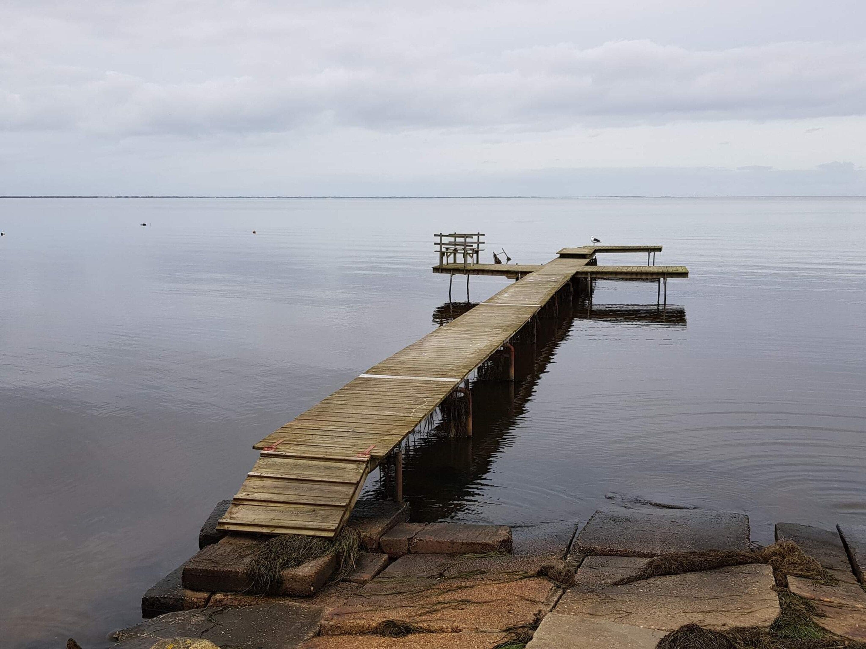 A wooden pier extending into calm water, with a bench and a small platform at the end.
