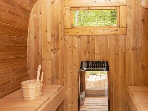 A sauna room with wooden walls, a window, a sauna heater, and a wooden bucket. - Vibrant Holiday Home in Tarm near Sea (Hemmet)