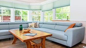 A cozy living room with a light blue sofa, a wooden coffee table, and a view of greenery through large windows. - Vibrant Holiday Home in Tarm near Sea (Hemmet)