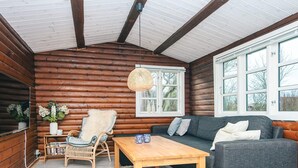 Ein gemütliches Blockhaus-Interieur mit einem Holztisch, einer Couch und einem Korbstuhl.