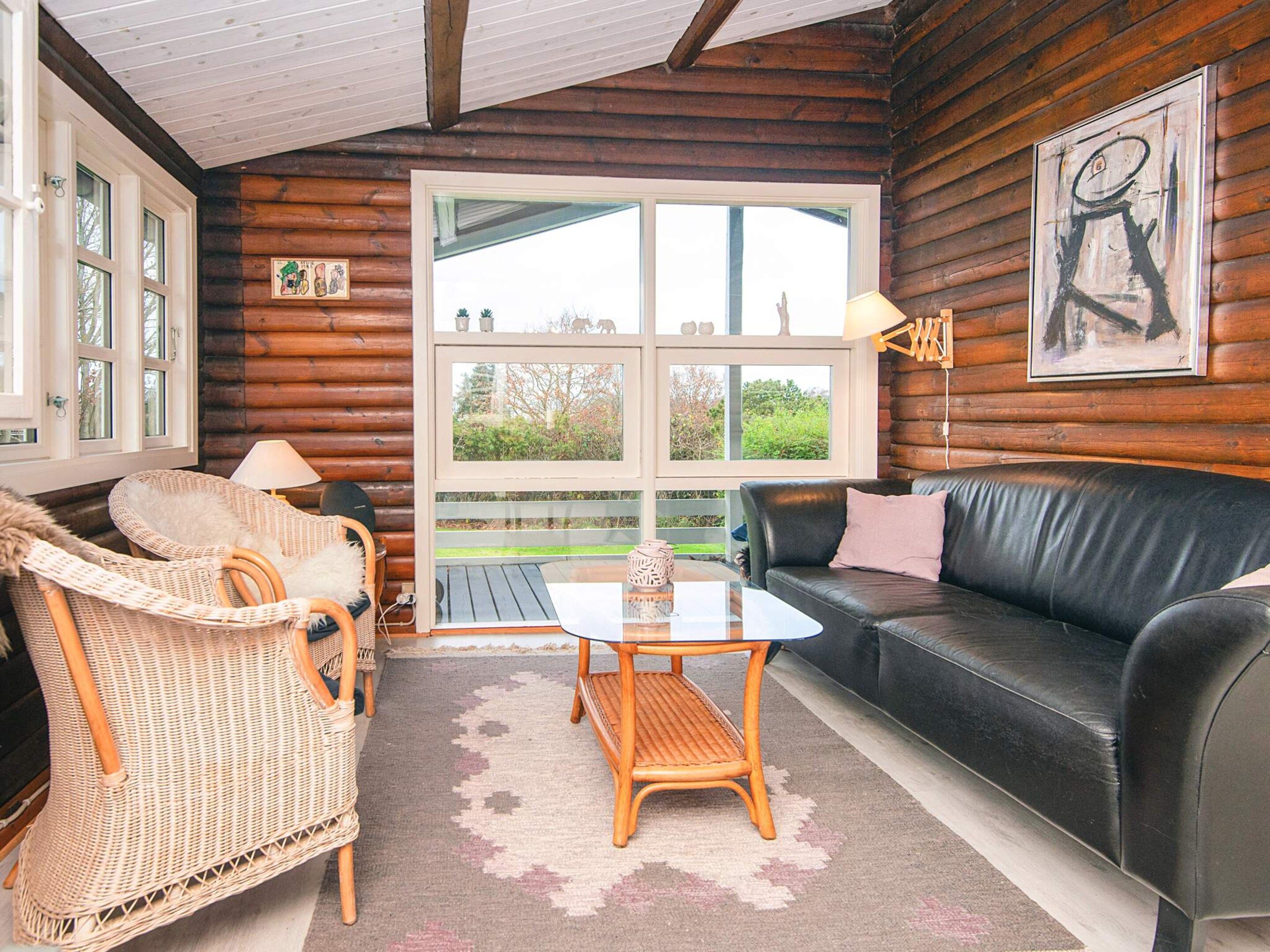 A cozy log cabin interior with a wicker chair, a leather sofa, and a table with a lamp.
