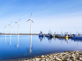 Una masa de agua tranquila con varias turbinas eólicas y barcos amarrados a la orilla.