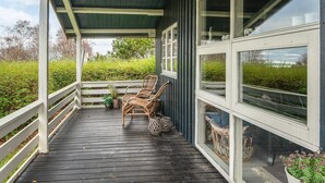 Eine überdachte Veranda mit Holzboden, Korbstühlen und Blick ins grüne Umland.