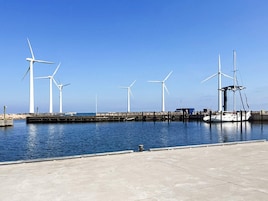 Marina con varias turbinas eólicas y un velero amarrado.