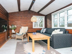 A log cabin interior with a sofa, a wooden table, a wicker chair, and a hanging light fixture. - Vibrant Holiday Home in Jutland near Sea (Glesborg)