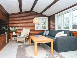 A log cabin interior with a sofa, a wooden table, a wicker chair, and a hanging light fixture.