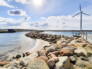 A coastal scene with a rocky breakwater, a wind turbine, and calm waters. - Vibrant Holiday Home in Jutland near Sea (Glesborg)
