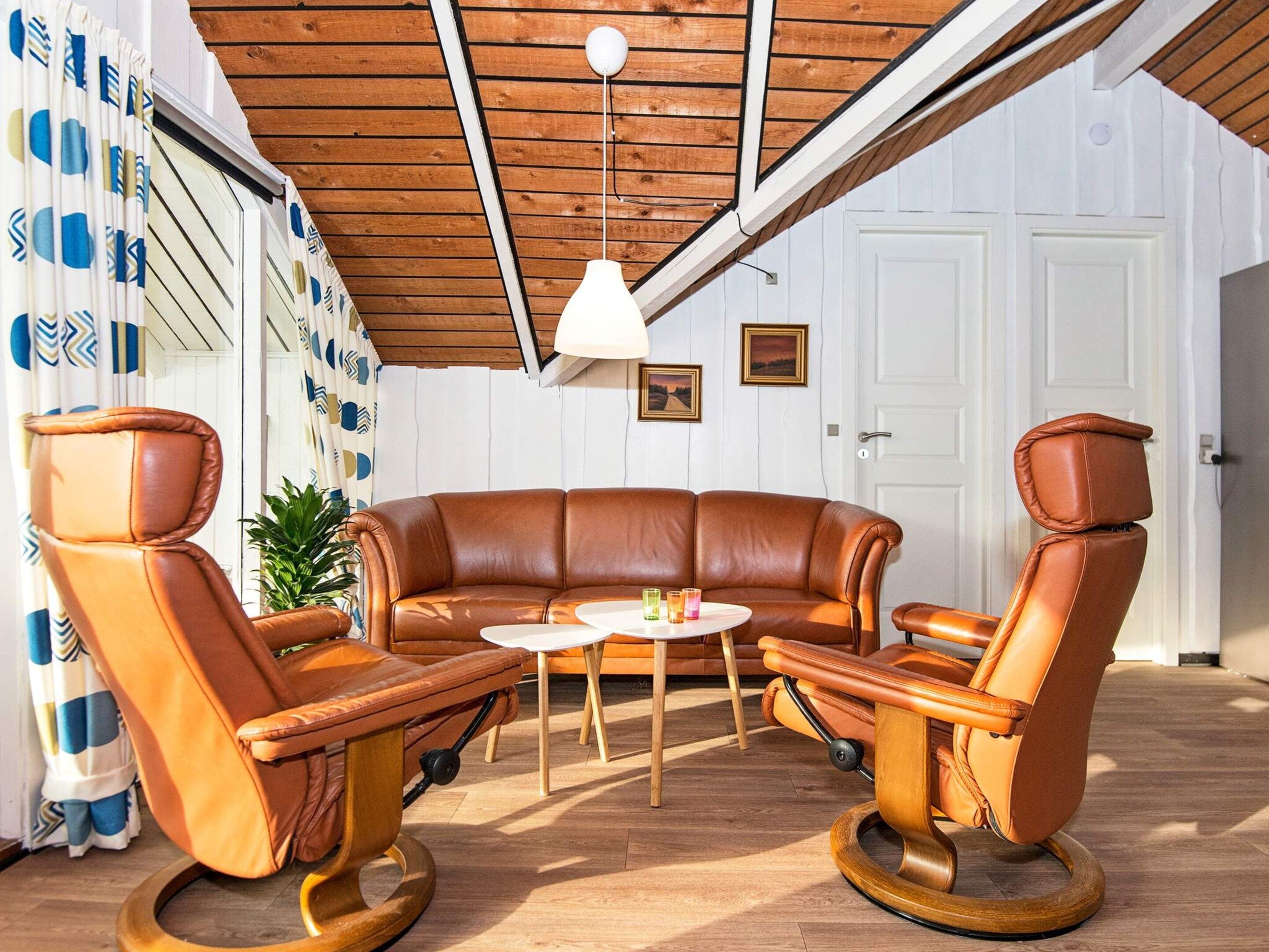 A room with a brown leather sofa, two leather armchairs, a small round table, and a ceiling light.
