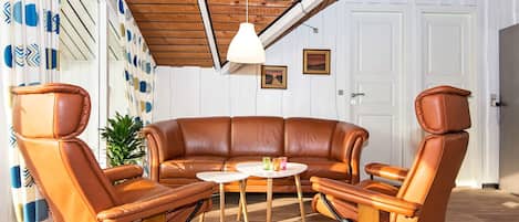 A room with a brown leather sofa, two leather armchairs, a small round table, and a ceiling light.