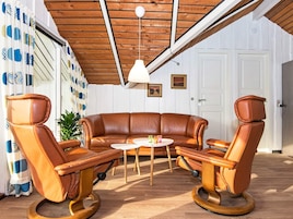 Una habitación con un sofá de cuero marrón, dos sillones de cuero, una mesita redonda y una lámpara en el techo.