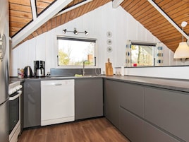 Una cocina compacta con lavavajillas, cafetera y ventana con cortinas.