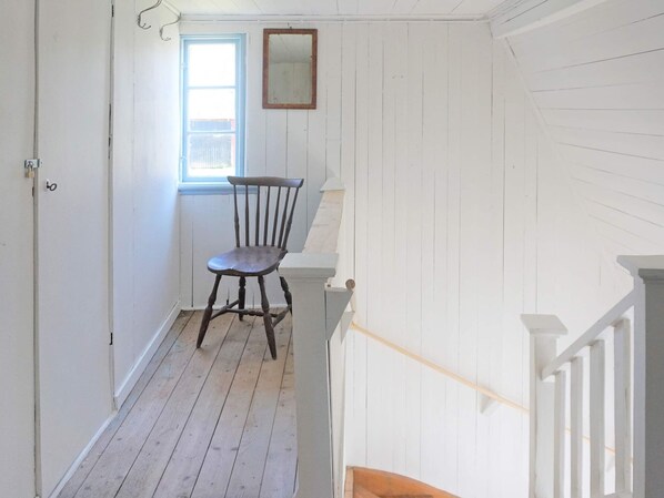 A narrow hallway with wooden flooring, a wooden chair, a window with a blue frame, and a white door. - 6 Person Holiday Home in Kyrkhult (Kyrkhult)