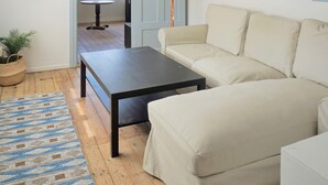 A living room with a beige sofa, a dark coffee table, a patterned rug, a potted plant, and a wall-mounted lamp. - 6 Person Holiday Home in Kyrkhult (Kyrkhult)
