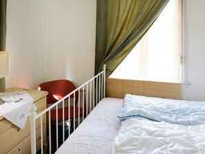 A small, simple room with a bed, a chair, a dresser, and a window with curtains. - 6 Person Holiday Home in Kyrkhult (Kyrkhult)