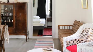 A room with a bed, a wicker chair, a small table with a bowl and magazines, and a cabinet with glass doors.
