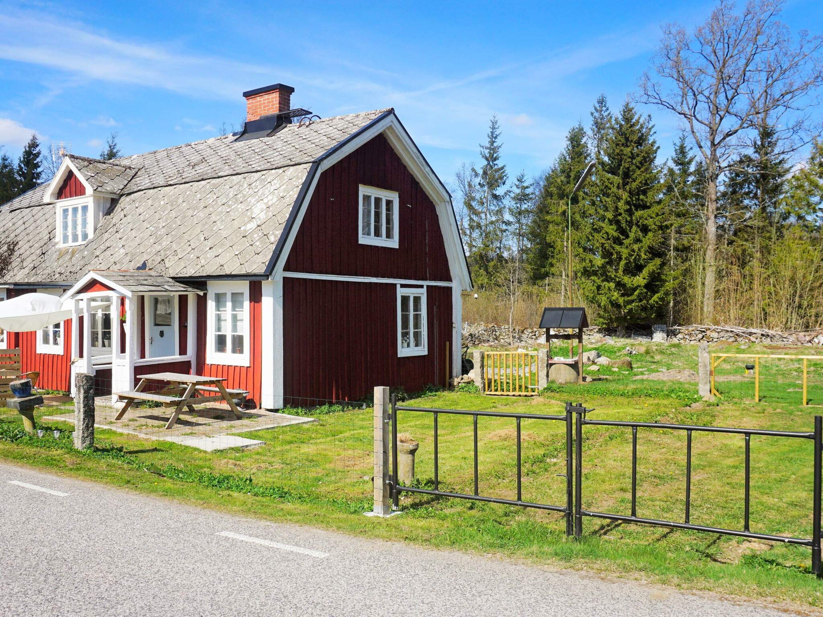 A red barn with a white door and windows, a picnic table, and a fenced yard with trees.