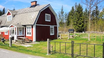 A red barn with a white door and windows, a picnic table, and a fenced yard with trees.