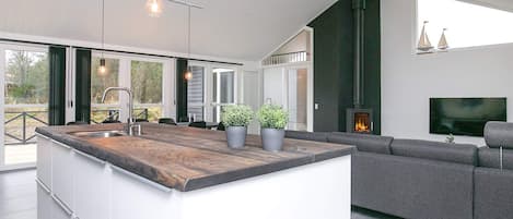 A modern kitchen with a large island, a built-in stove, and a dining area with a sofa and TV.