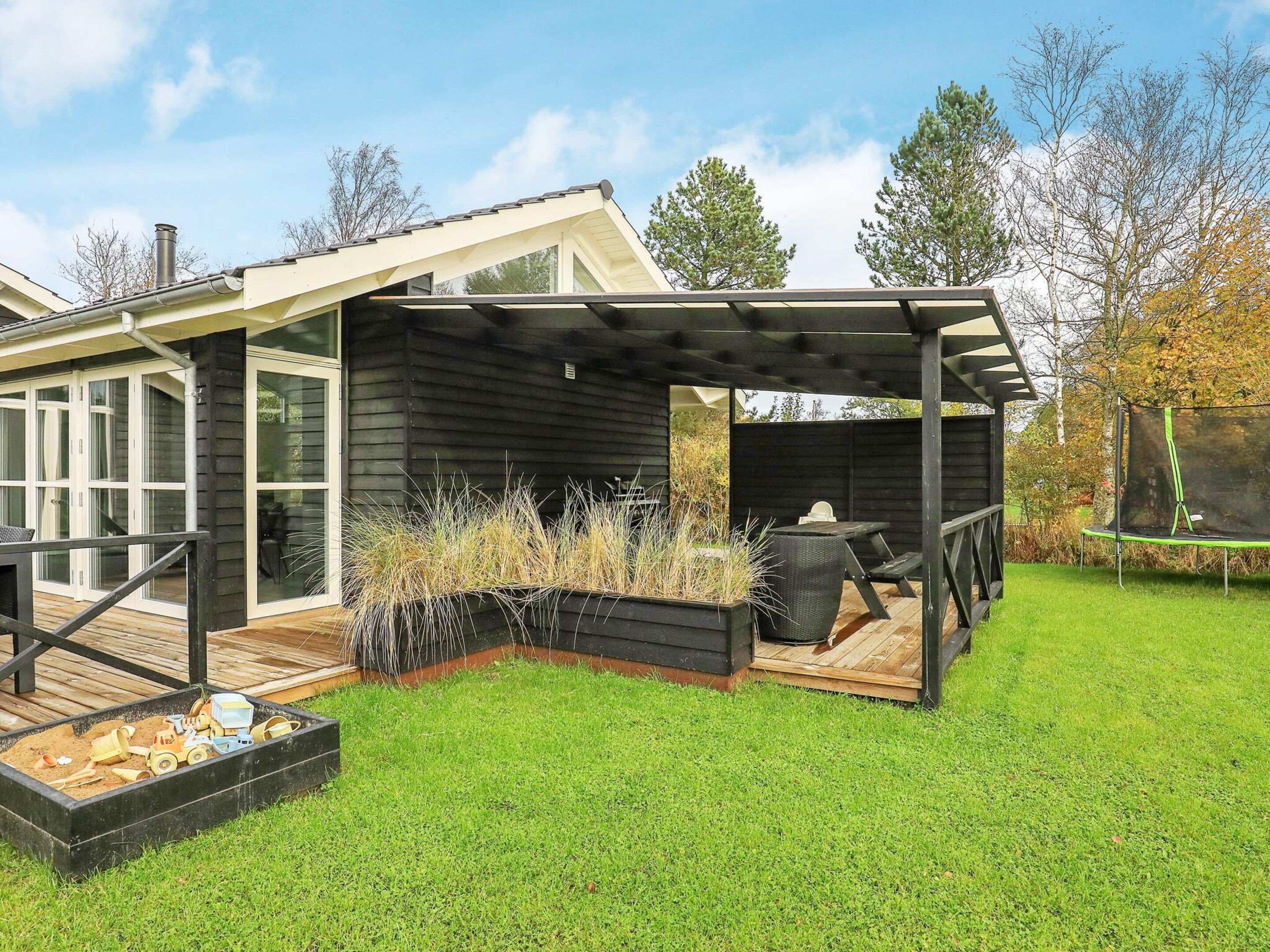 A modern house with a covered patio, a wooden deck, and a trampoline.