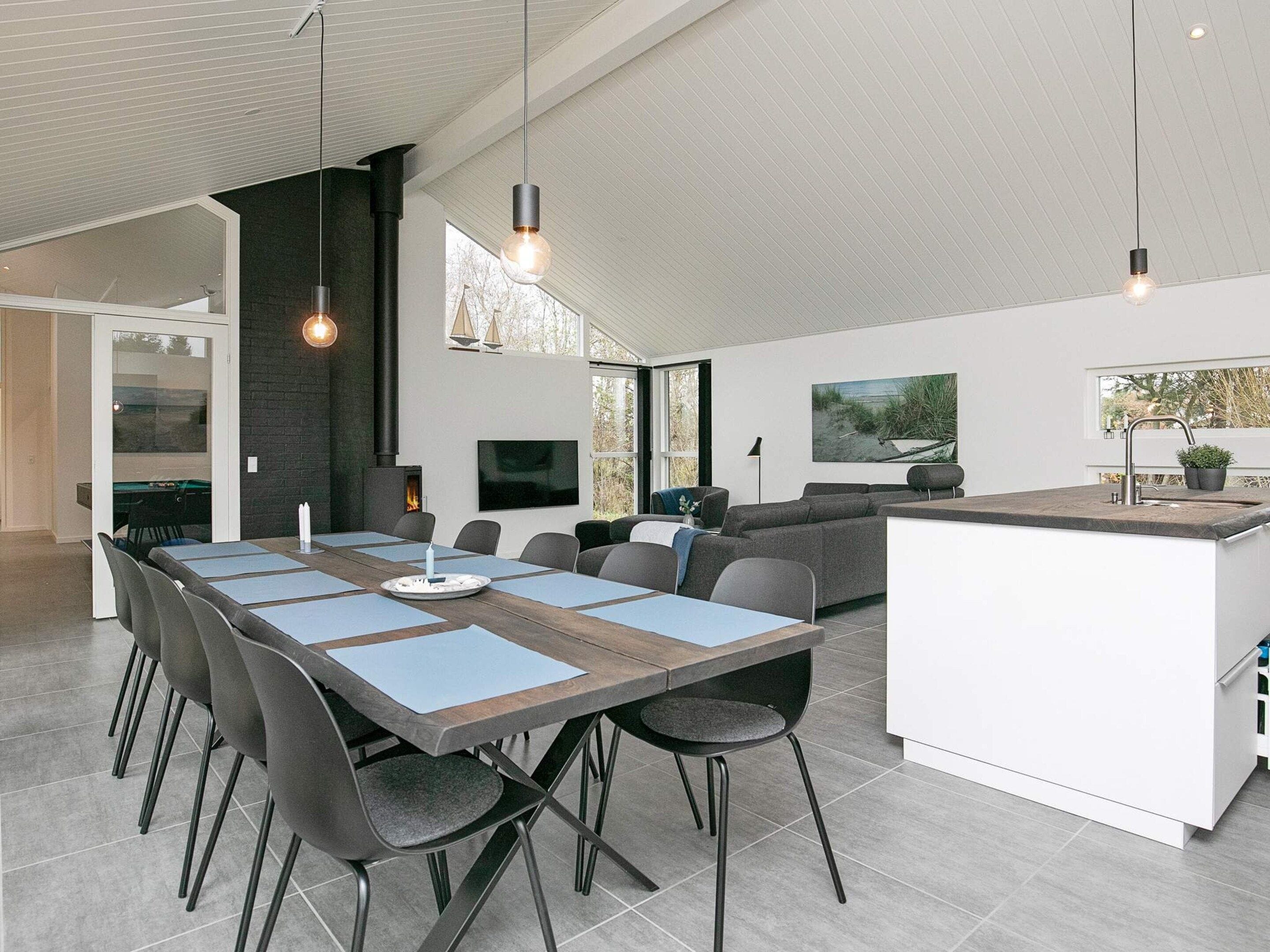Una cocina moderna con una isla central, un comedor con una mesa larga y sillas, y una chimenea empotrada.