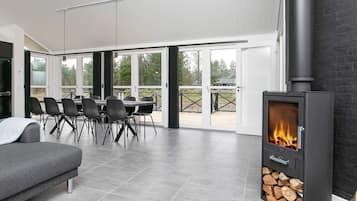 Una sala moderna con chimenea, un sofá, una mesa de comedor con sillas y ventanas grandes.