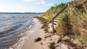 A beach with a wooden staircase leading down to the shore, surrounded by seaweed and grasses. - Seaside Serenity in Teglgarden-by Traum (Hejls)