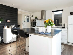 A modern kitchen with a central island, bar stools, a stainless steel range hood, and a window with a view. - 8 Person Holiday Home in Hejls (Hejls)