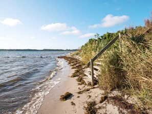A beach with a wooden staircase leading down to the water, surrounded by grass and seaweed. - 8 Person Holiday Home in Hejls (Hejls)