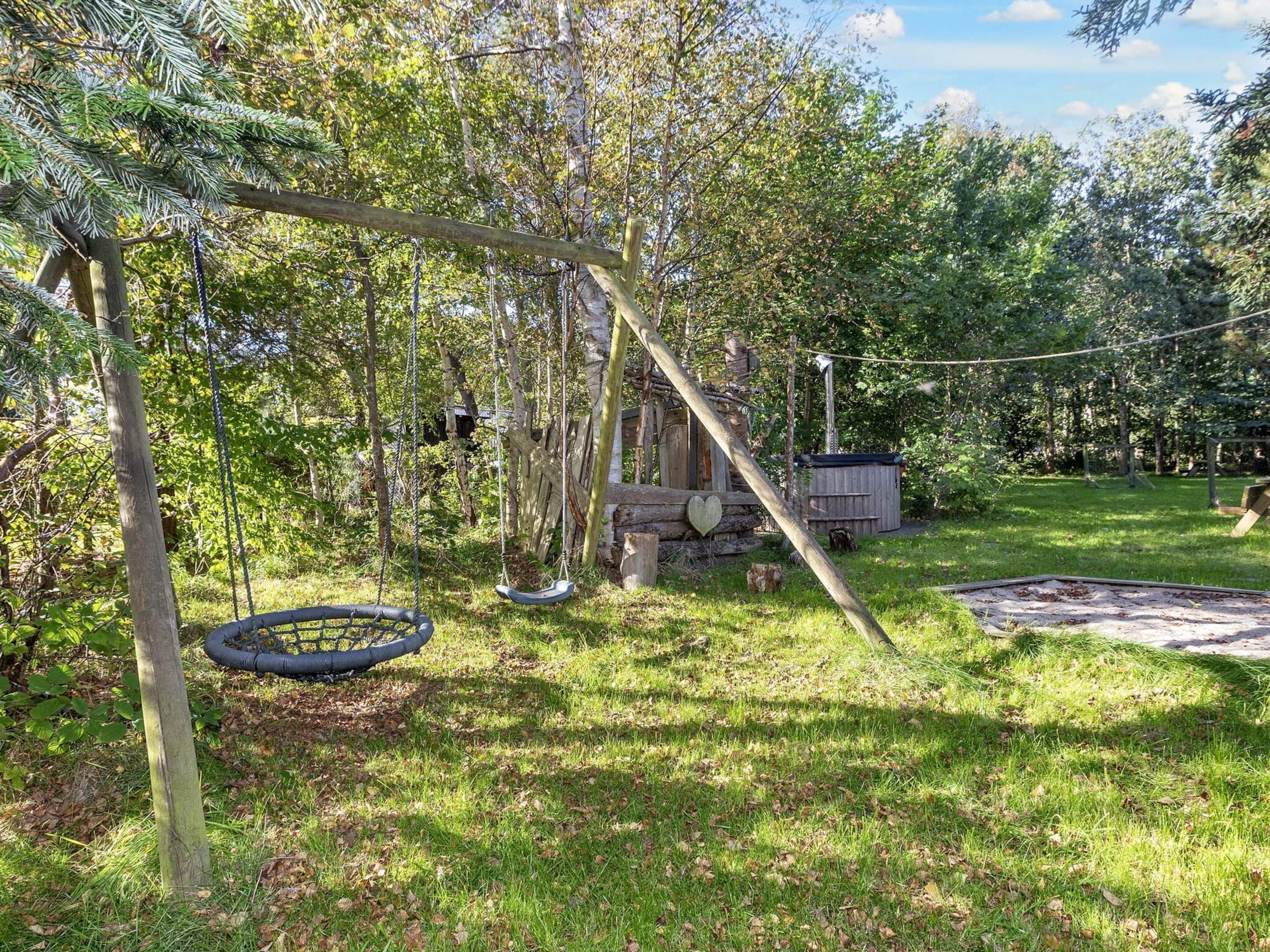 Un patio trasero con un conjunto de columpios, un neumático colgante y una pequeña construcción de madera.