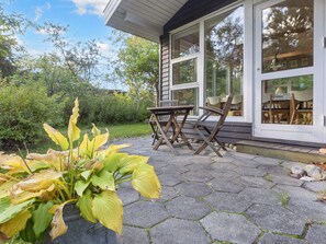 A patio with a table and chairs, a potted plant, and a house with large windows. - 8 Person Holiday Home in Thyholm (Thyholm)