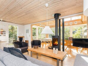 A modern living room with a large wooden table, comfortable seating, a fireplace, and large windows. - 8 Person Holiday Home in Thyholm (Thyholm)