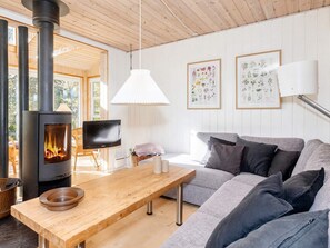 A cozy living room with a wood-burning stove, a sofa, a wooden table, and framed botanical prints on the wall. - 8 Person Holiday Home in Thyholm (Thyholm)