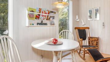 A room with a round table, white chairs, a rocking chair, a shelf with children's books, and framed artwork on the wall.