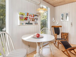 A room with a round table, white chairs, a rocking chair, a shelf with children's books, and framed artwork on the wall. - 8 Person Holiday Home in Thyholm (Thyholm)