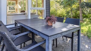 An outdoor patio with a table and chairs, a potted plant, and a view of a house through large windows. - 8 Person Holiday Home in Thyholm (Thyholm)
