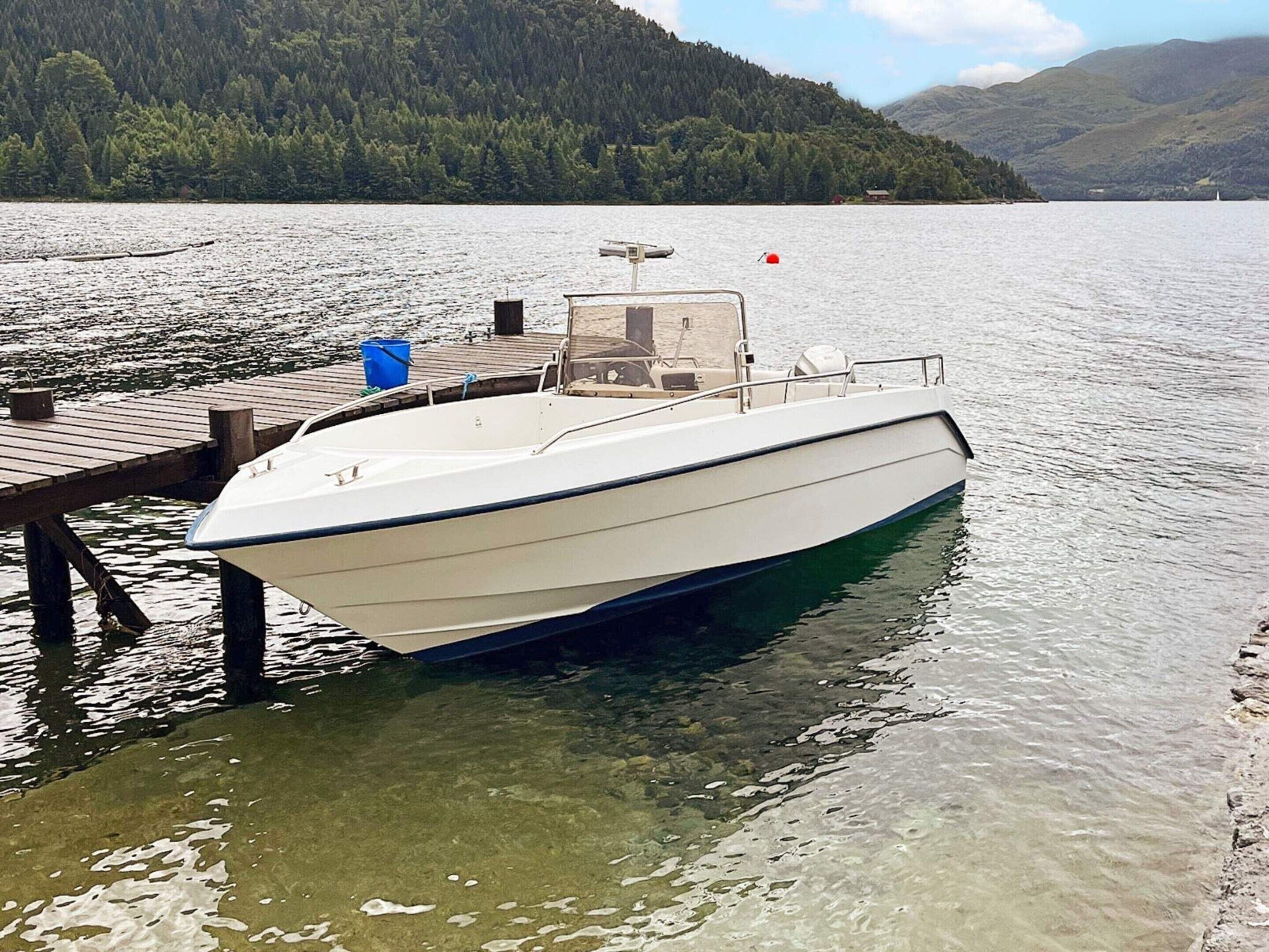 A boat docked at a wooden pier with a forested mountain backdrop.