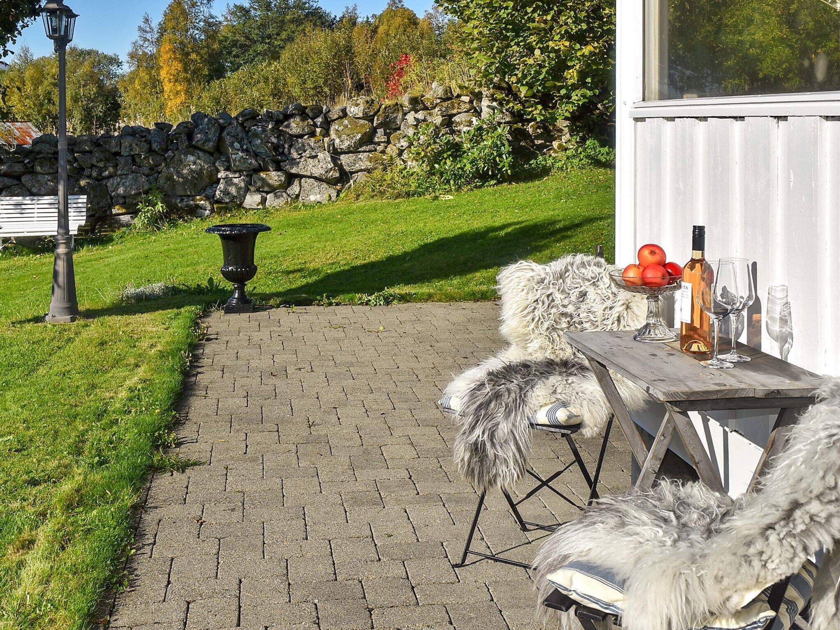 Un muro de piedra, una zona con césped, un banco de madera, una mesa con una botella y vasos, y un perro.