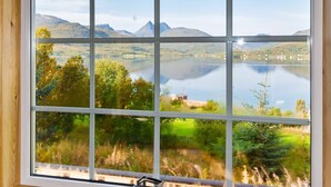 A window with a view of a lake, mountains, and greenery. - 4 Person Holiday Home in Botnhamn (Senja)