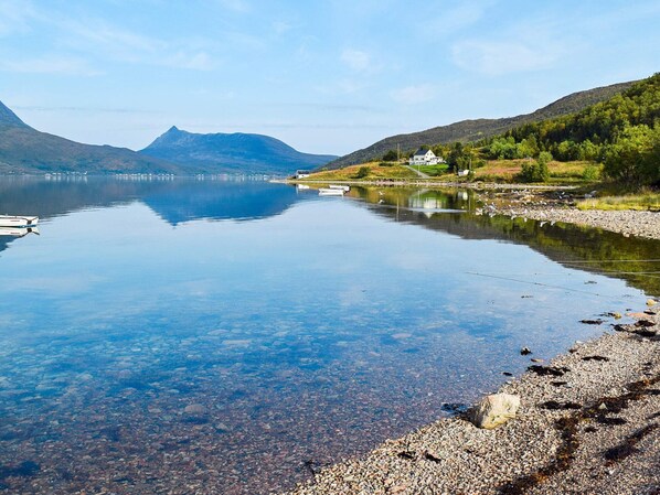 A calm lake with a clear view of a mountain in the distance, a small house on the shore, and a boat docked nearby.