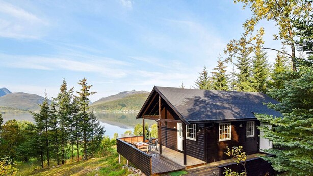A cabin with a deck overlooking a lake, surrounded by trees and mountains. - 4 Person Holiday Home in Botnhamn (Senja)