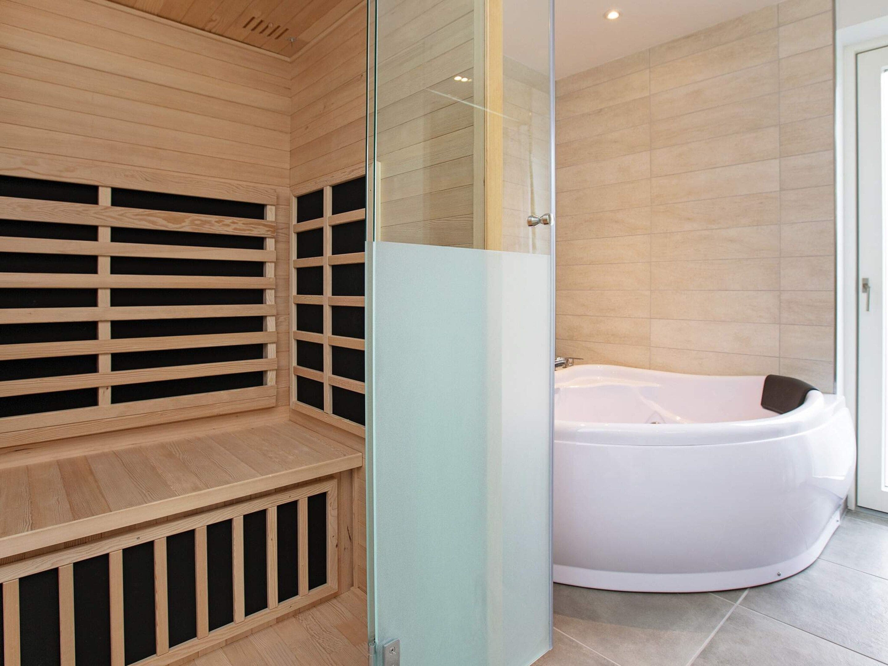 A modern bathroom with a wooden sauna, a glass shower enclosure, and a white bathtub.