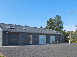 A modern building with a sloped roof, large windows, and a gravel driveway. - 5 Star Holiday Home in Dannemare (Dannemare)