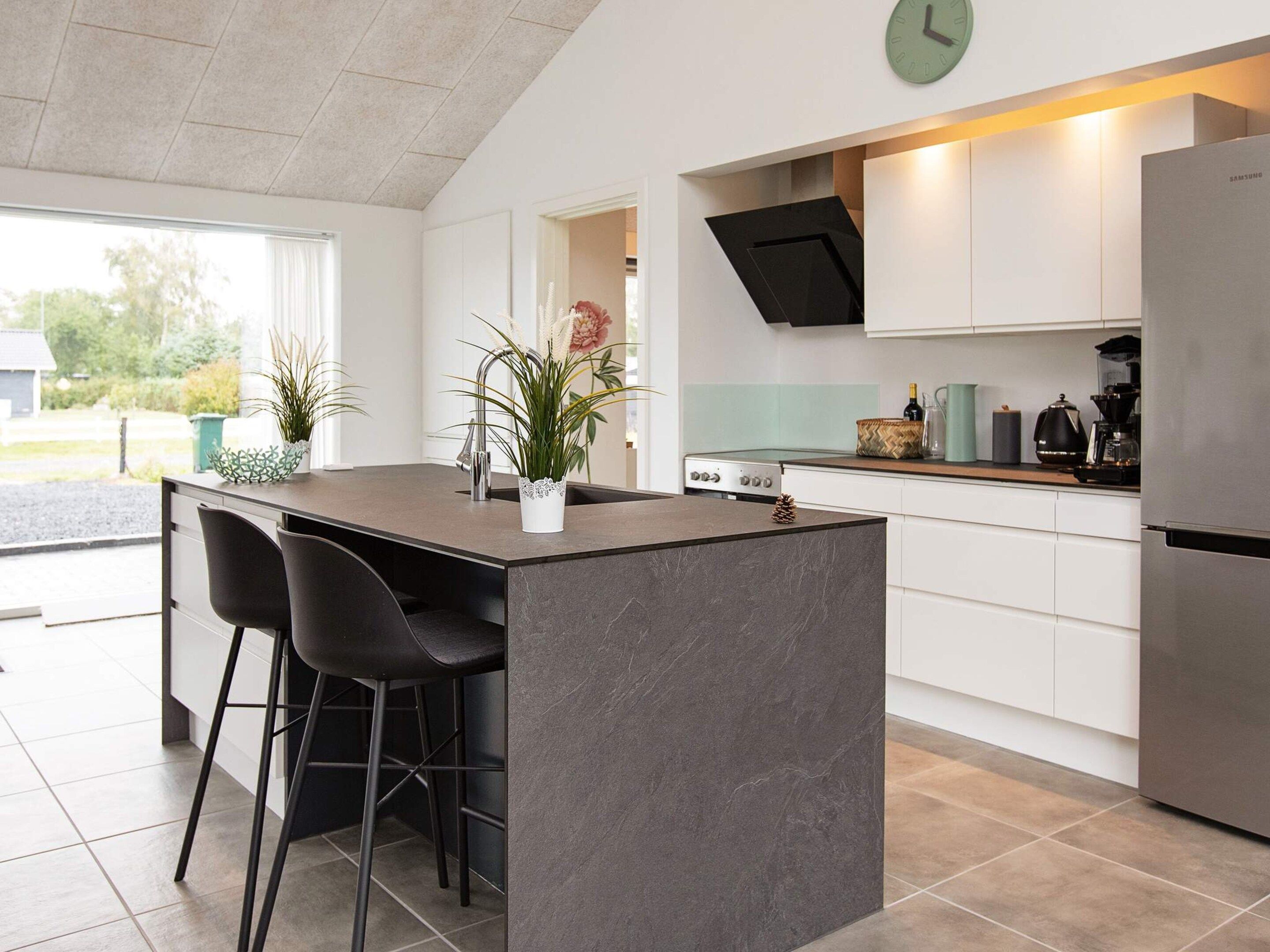 A modern kitchen with a central island, bar stools, a stainless steel refrigerator, and a clock on the wall.