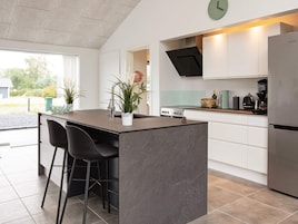 Una cocina moderna con una isla central, taburetes de bar, un refrigerador de acero inoxidable y un reloj en la pared.