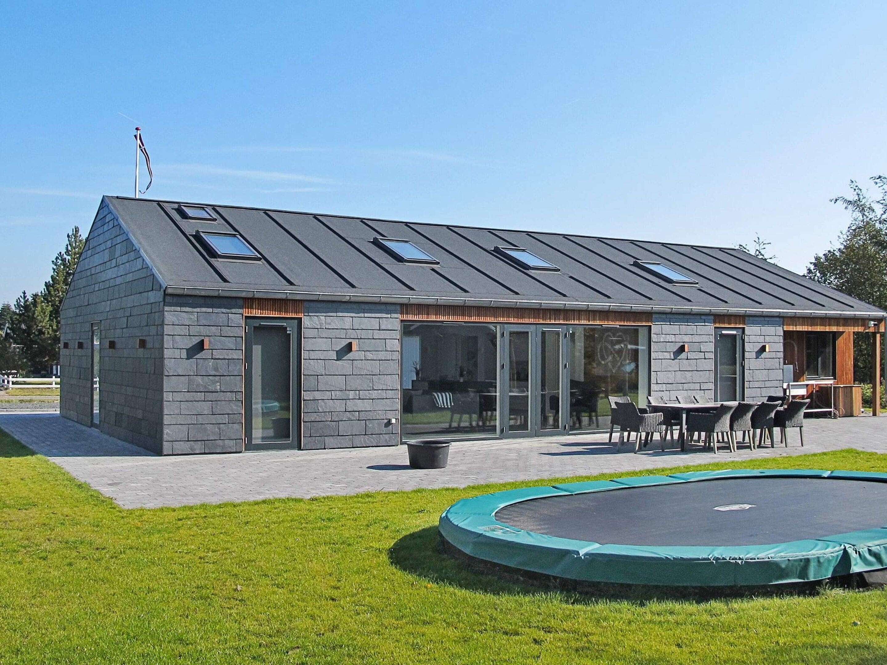 A modern building with a sloped roof, large glass windows, and a covered outdoor seating area.