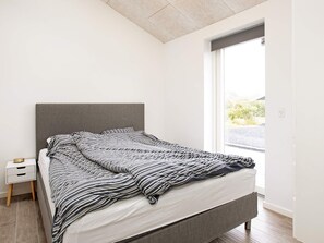 A modern bedroom with a bed, a nightstand, and a window. - 5 Star Holiday Home in Dannemare (Dannemare)