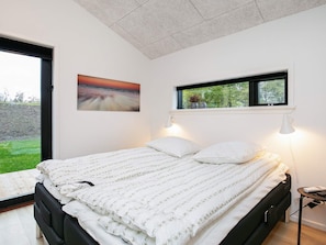 A bedroom with a bed, two bedside lamps, a window with a view, and a painting on the wall. - 5 Star Holiday Home in Hjorring (Hjørring)
